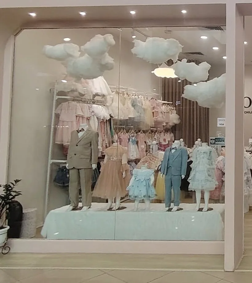Bonny Billy window display of pastel occasion dresses under soft cloud décor